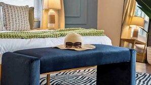 A bedroom with a bed, a blue ottoman, a lamp, and a window with blinds. - Hot Tub - Family - Dogs Allowed - Arcade Machine -MegaChess STR-A-25-00194 (St. Petersburg)