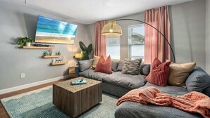A modern living room with a large flat-screen TV, a grey sofa, a coffee table, and a floor lamp. - Hot Tub - Family - Dogs Allowed - Arcade Machine -MegaChess STR-A-25-00194 (St. Petersburg)