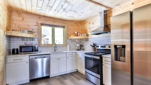 A compact kitchen with wooden walls, a stainless steel refrigerator, a microwave, a dishwasher, and a stove.