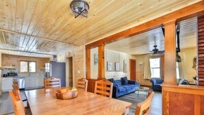 A spacious wooden interior with a large dining table, a kitchen area, and a living room with a blue sofa.