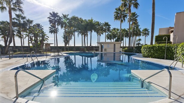 A swimming pool with clear blue water, surrounded by palm trees and a lifeguard station. - Penthouse Bahia de la Plata (Estepona)