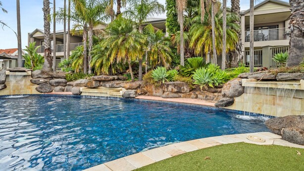 Une piscine bordée de pierres, entourée de plantes tropicales et de palmiers.