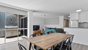 Une cuisine moderne avec des meubles blancs, un coin repas avec une table et des chaises en bois, un téléviseur et un canapé.