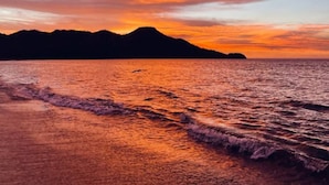 A sunset over a beach with waves, mountains in the background, and a clear sky. - Bay Point 7 • 3 BR Ocean-View Condo • Two Infinity Pools, Playa Panamá - 6 Guests (Playa Hermosa)