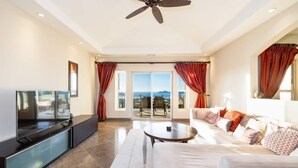 A spacious living room with a flat-screen TV, a sofa, a coffee table, and a ceiling fan. - Bay Point 7 • 3 BR Ocean-View Condo • Two Infinity Pools, Playa Panamá - 6 Guests (Playa Hermosa)