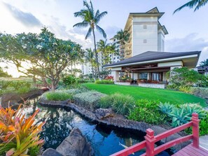 A modern hotel with a pool, lush greenery, and a red bridge. - Hale Keani O-1203 stunning Views to relax: Special book 7 NIGHTS in September AND GET 1 NIGHT FREE (Kapolei)