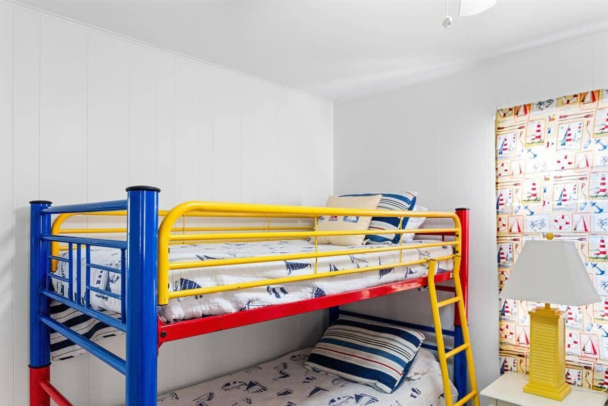Un lit superposé avec une échelle, une table de chevet avec une lampe et un mur recouvert d’un papier peint à motifs.