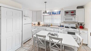 Une cuisine moderne avec des meubles blancs, une cuisinière à gaz, un four à micro-ondes et un coin repas comprenant une table et des chaises blanches.