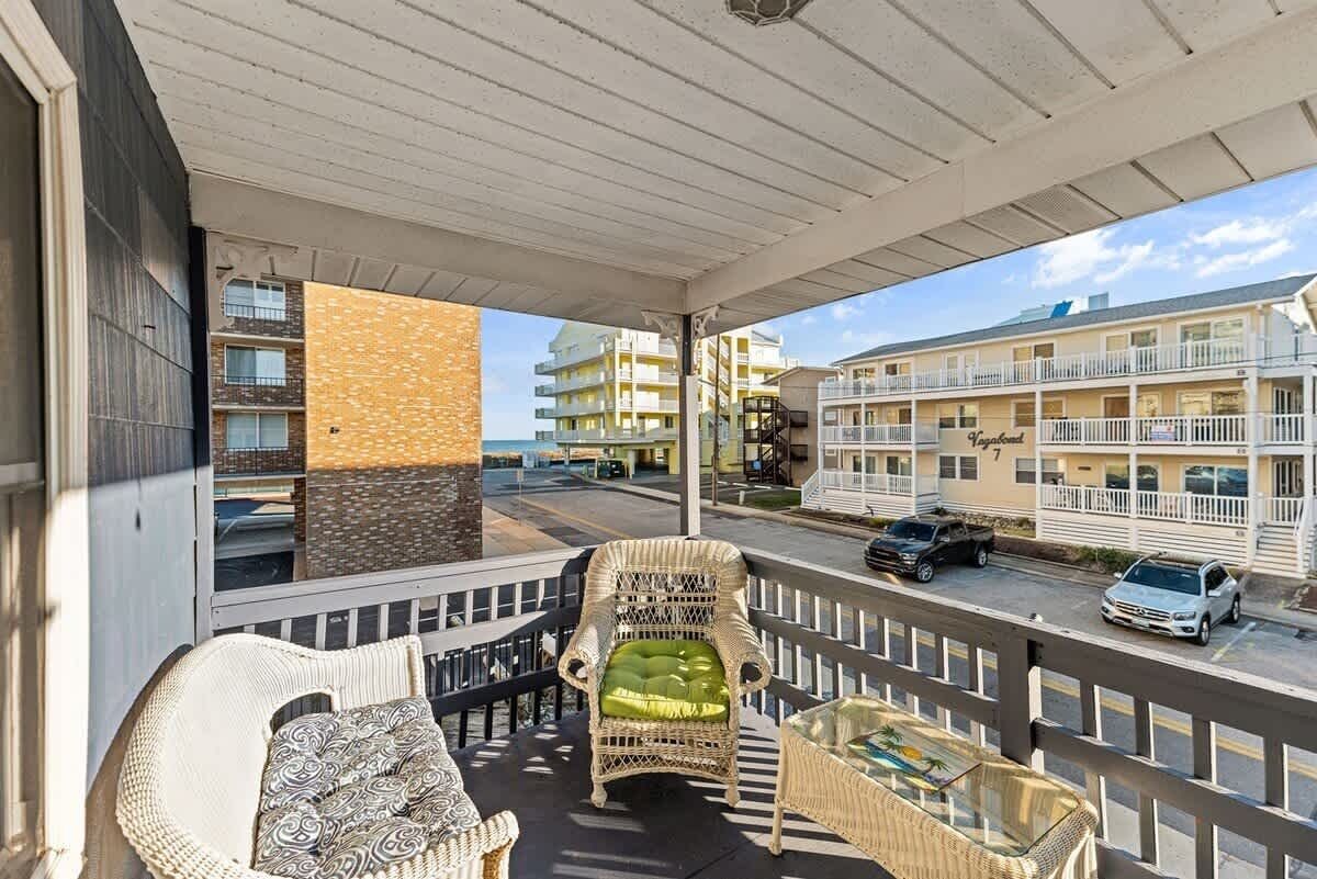 A balcony with wicker furniture, a view of a multi-story building, and a street with parked cars.