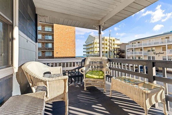 A balcony with wicker furniture, a glass table, and a view of buildings. - Beach Block 3BR Condo w/Ocean View (Ocean CIty)