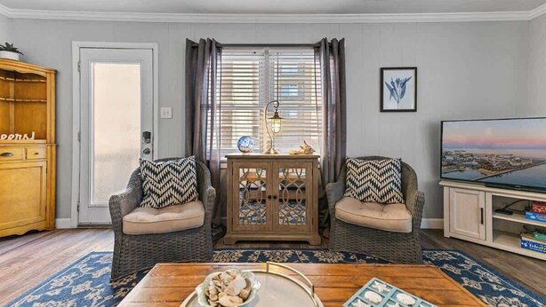 Una sala de estar con un conjunto de sofá, una mesa de centro, un mueble, un televisor y una ventana con cortinas.
