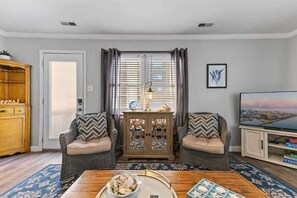 A living room with a sofa set, a coffee table, a cabinet, a television, and a window with curtains. - Beach Block 3BR Condo w/Ocean View (Ocean CIty)