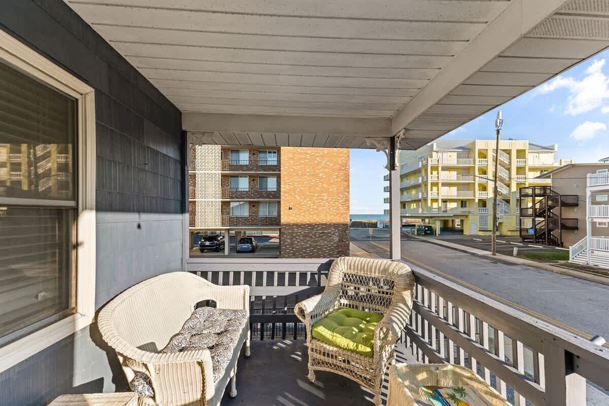 Un balcon agrémenté de meubles en osier, une vue sur un immeuble à la façade ornée, et un ciel dégagé.