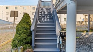 A staircase leading to a building with a modern design, a small tree, and a clear sky.