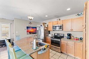 A kitchen with a central island, stainless steel appliances, wooden cabinets, and a painting on the wall.