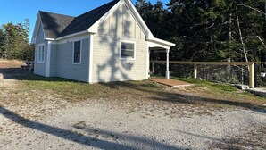 A small, single-story house with a gabled roof, a covered porch, and a gravel driveway. - The Bodwell Cottage at East Boston Quarry (Vinalhaven)