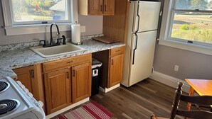A kitchen with wooden cabinets, a white refrigerator, a sink, and a stove. - The Bodwell Cottage at East Boston Quarry (Vinalhaven)