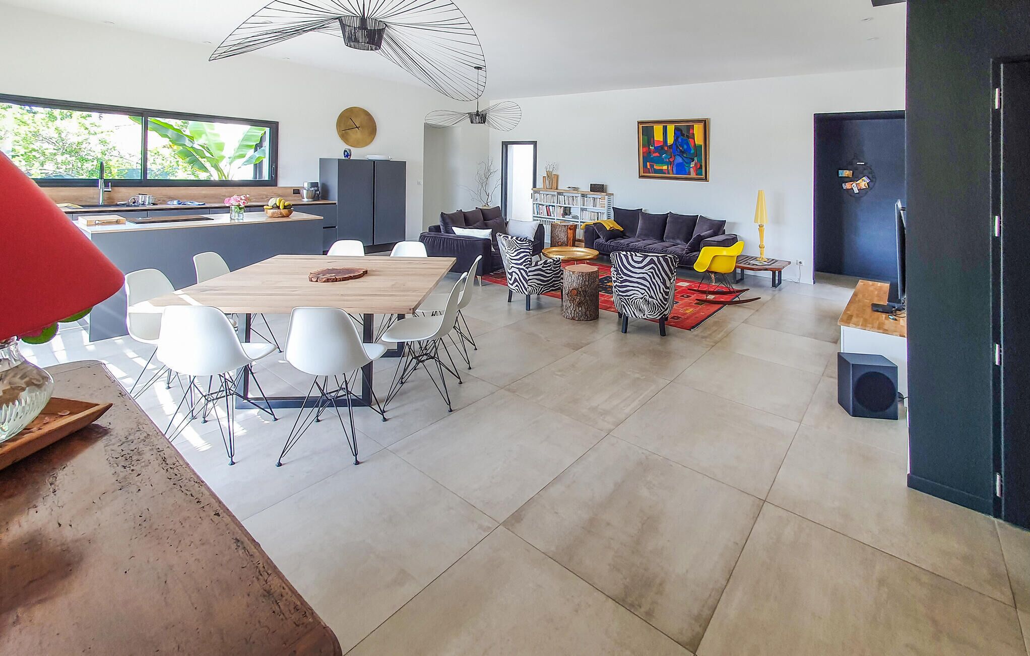 A spacious living area with a dining table, modern chairs, a sofa set, and a bookshelf.