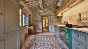 Un pasillo estrecho con piso estampado que conduce a una zona de cocina con pared de piedra y vigas de madera.