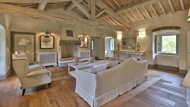 Amplia habitación con techo de madera alta, un sofá blanco grande, una silla de mimbre y un tocador con espejo.