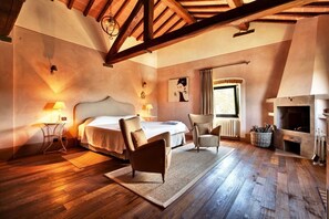 Cozy bedroom with a large bed, bedside tables, and a fireplace, featuring exposed beams and a window.