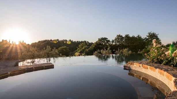 A tranquil infinity pool with a stone edge, surrounded by lush greenery and a clear sky.