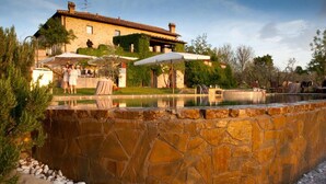 A stone pool with a stone wall, outdoor umbrellas, and a building in the background.