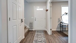 A hallway with a white door, a black metal rack, and a patterned rug. - Modern, Spacious Whole Unit Traveler's Home! (Fort Wayne)