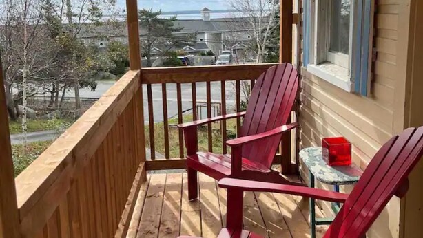 A wooden deck with two red Adirondack chairs and a small table.