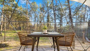 Eine Holzterrasse mit Tisch und zwei Korbstühlen mit Blick auf einen Wald.