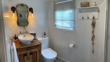 A bathroom with a wooden vanity, white sink, and a large mirror. There is a toilet and a window with curtains.