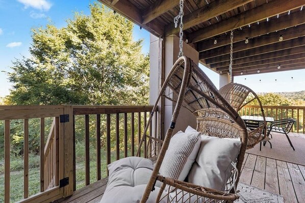 A wooden deck with a hanging chair and a table, overlooking a natural landscape.