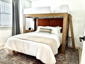 A neatly made bed with a wooden headboard, a patterned rug, and a bedside table with a lamp.