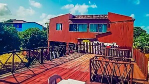 Une terrasse en bois mène à un bâtiment rouge sur lequel on peut lire l’inscription « Hôtel ».