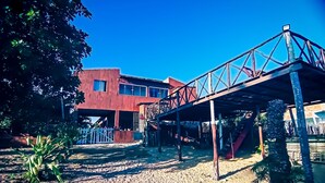 Un edificio con facciata rossa, una zona esterna coperta con un ponte in metallo e terreno sabbioso.