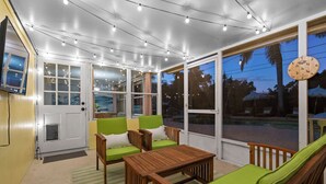Un solárium con una mesa y sillas de madera, ventanas amplias y luces colgantes.