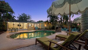 Zona de piscina con sillas de descanso, una piscina y una casa con puertas de cristal.