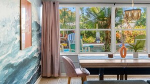 Una habitación con un ventanal grande, una mesa de madera, una silla rosa y un jarrón decorativo.