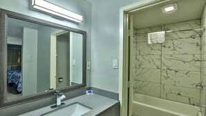 Une salle de bain dotée d’un grand miroir, d’un lavabo et d’un espace douche aux carreaux de marbre.