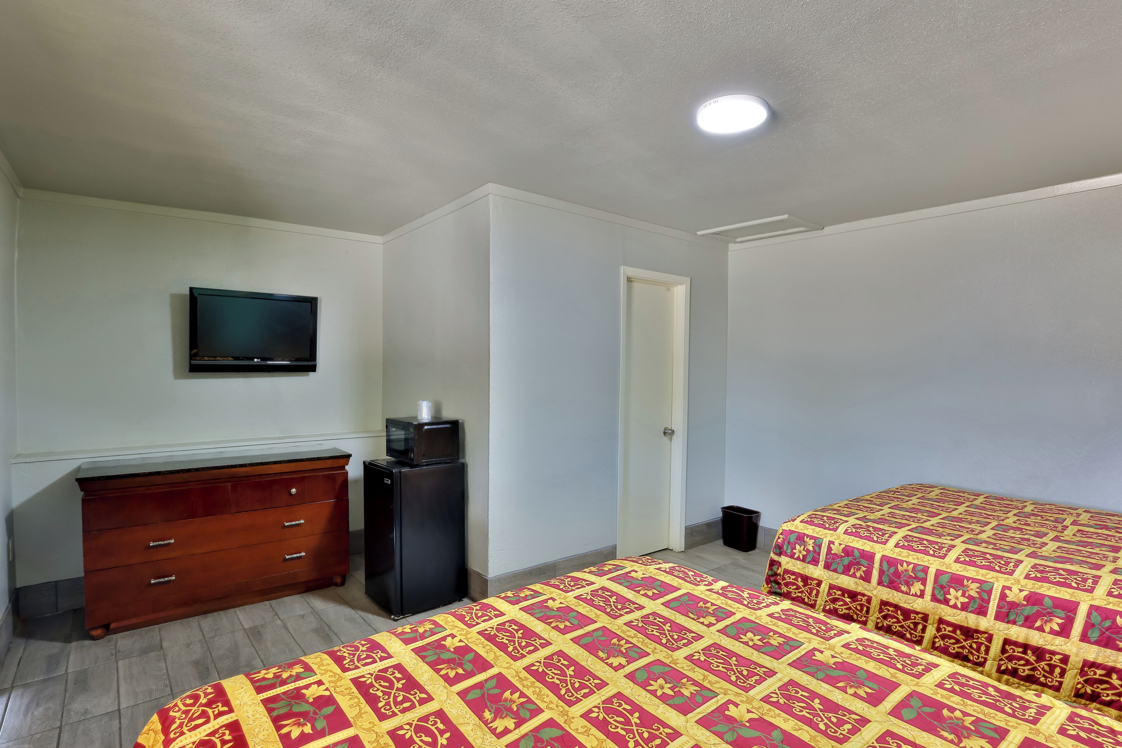 A bedroom with two beds, a dresser, a television, and a small refrigerator.