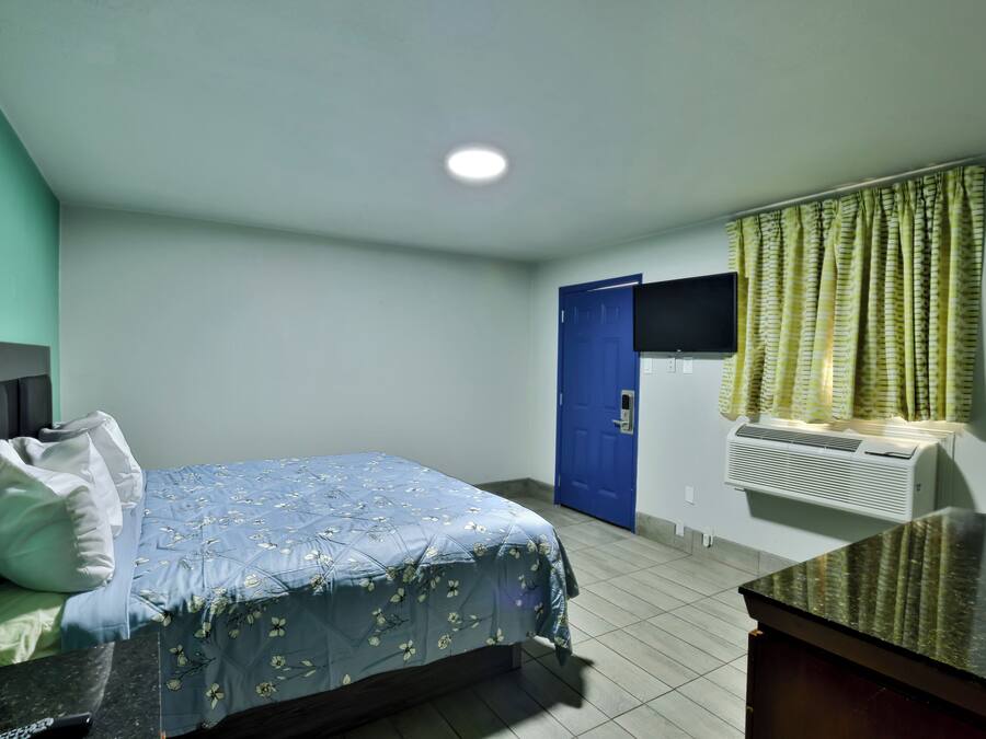Een hotelkamer met een bed, een flatscreen-tv aan de muur, een blauwe deur en een airconditioner.