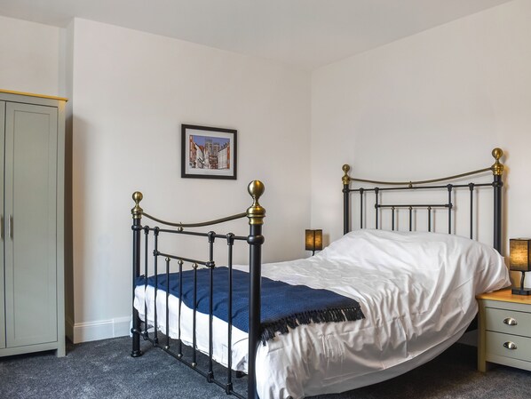 A bedroom with a single bed, a nightstand, a lamp, a wardrobe, and a framed picture on the wall.