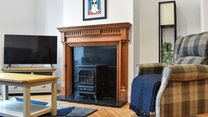 Een woonkamer met een open haard, een televisie, een bank en een ingelijste foto aan de muur.