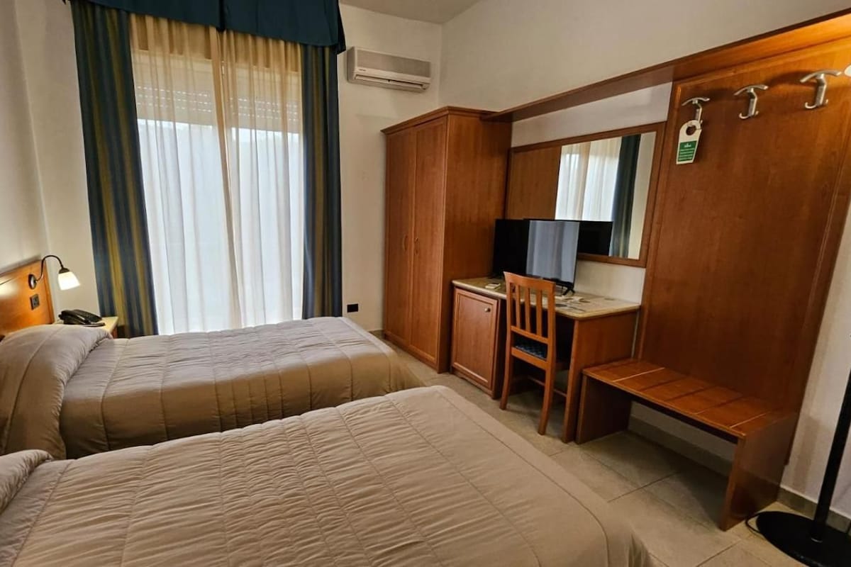 A hotel room with two beds, a desk, a chair, a mirror, and a wardrobe.