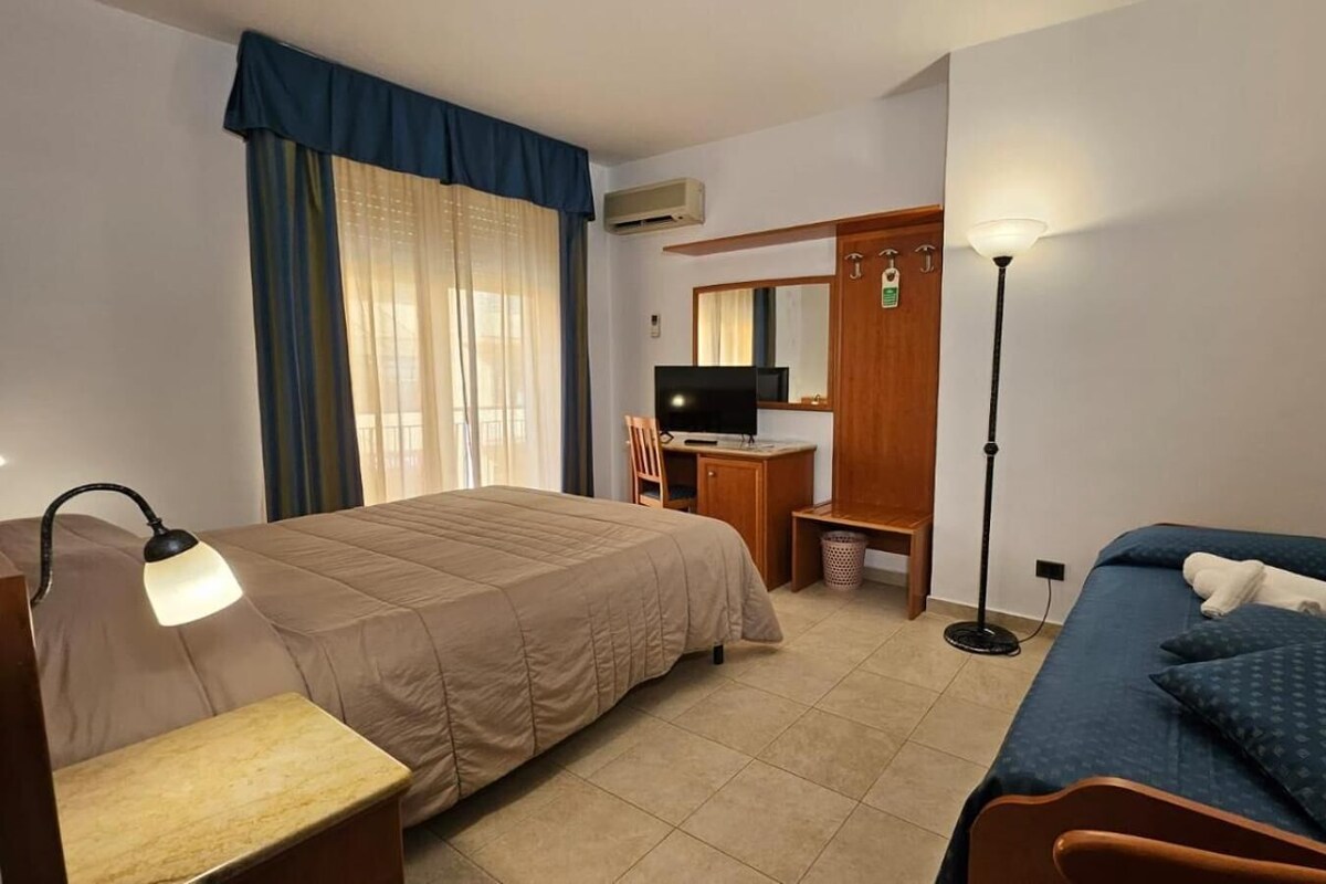 A hotel room with a bed, a desk, a chair, a lamp, and a wardrobe.