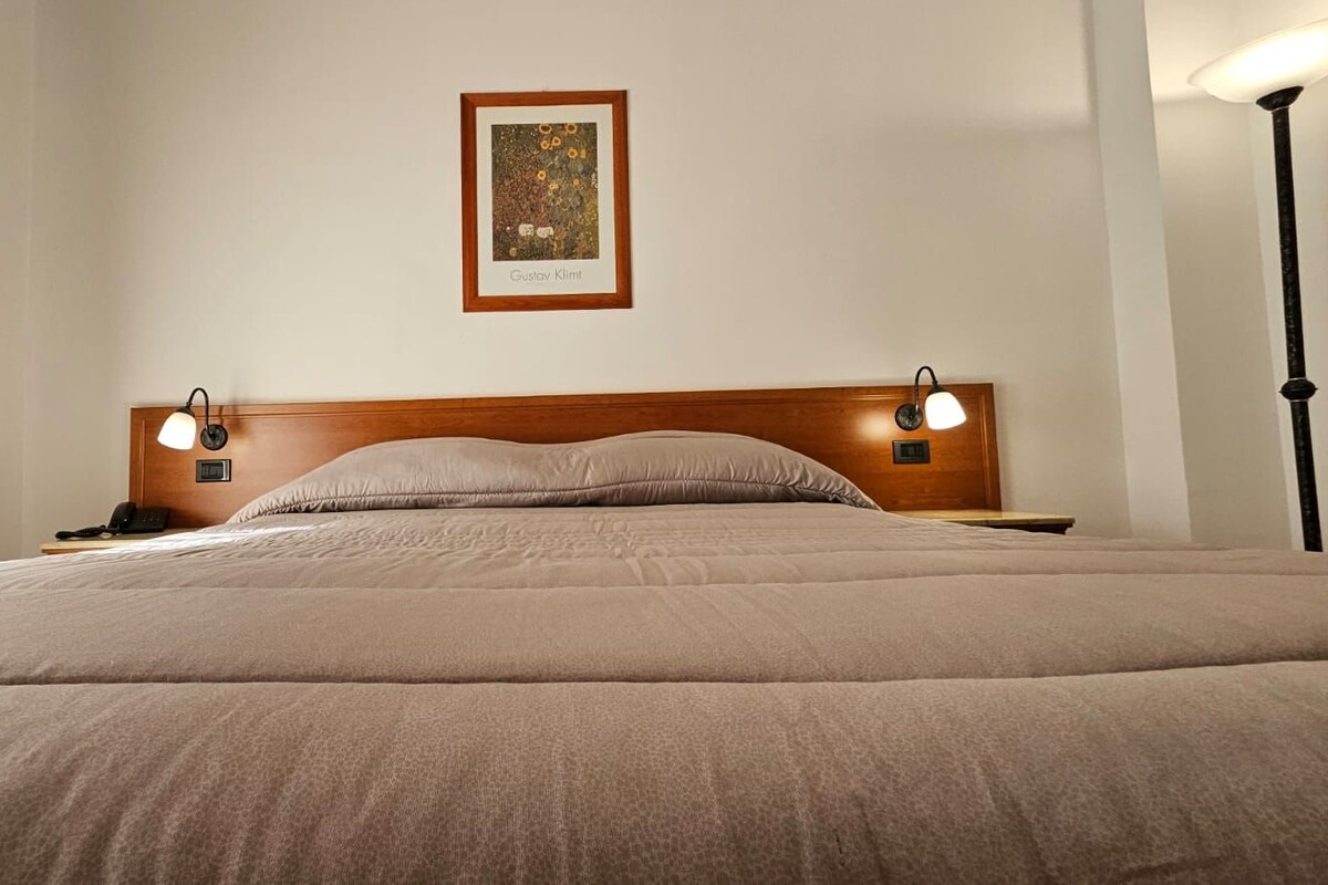 A neatly made bed with a headboard, two bedside lamps, and a framed artwork on the wall.