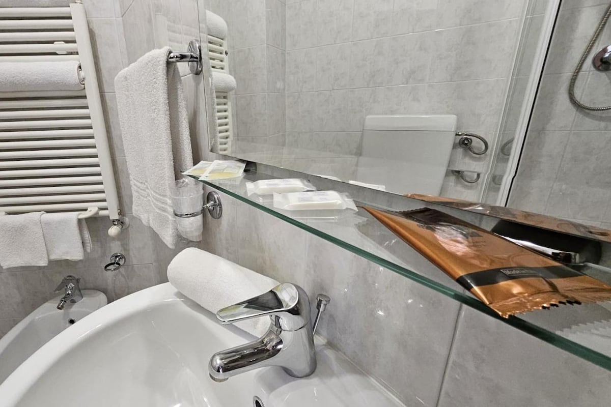 A bathroom with a glass shower enclosure, a white bathtub, and a glass-topped vanity with toiletries.