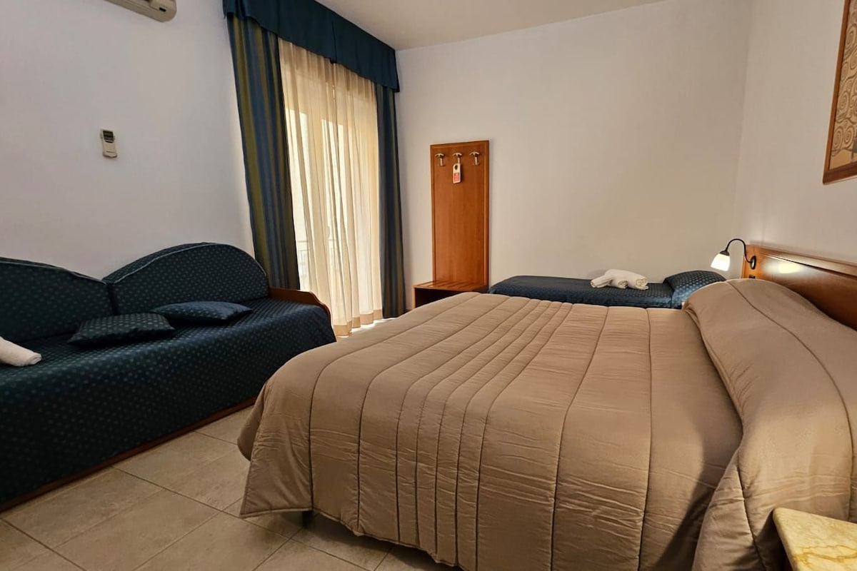 A hotel room with a bed, a sofa, a desk, and a wardrobe.