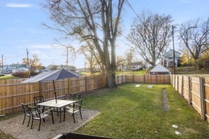 Ein Garten mit Holzzaun, einem Tisch mit Stühlen und einer überdachten Terrasse.