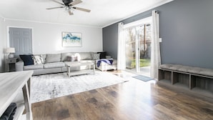 A spacious living room with a grey sofa, a coffee table, and a bench by the sliding glass door.